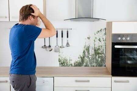 man shocked on seeing mold on wall in kitchen